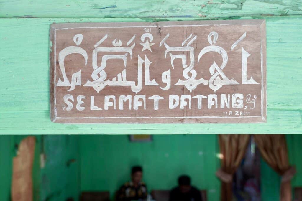 Papan dengan aksara jawa & kaligrafi arab bertuliskan ‘Selamat Datang’ menyambut di pintu masuk PBM (Pusat Belajar Mengaji) Yanbuul Qur’an Yaqu, Desa Padas, Kedungjati, Grobogan.
