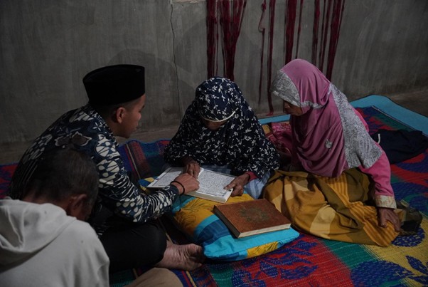 Ustaz Sya’ban sedang menyimak bacaan tilawah Al-Qur’an yang lantunkan warga saat Ia berkunjung berdakwah dari pintu ke pintu di Kabupaten Samosir,