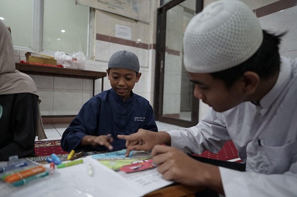 Two boys wearing caps coloring and playing with markers at a low table.