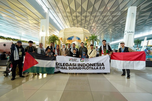 Indonesian delegation at an airport holding a banner for Global Sumud Flotilla 2.0, with Palestinian and Indonesian flags on either side.