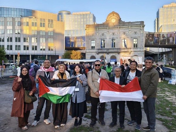 kongres parlemen gsf 2026 1 dompet dhuafa Group of diverse adults posing with Palestinian and Indonesian flags in a city square, with a historic building and modern glass towers behind them.