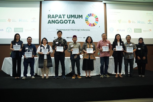 penghargaan penghimpunan filantropi indonesia 4 dompet dhuafa Eleven people on a stage at a conference, each holding a certificate, with a banner reading 'Rapat Umum Anggota' and logos in the background.