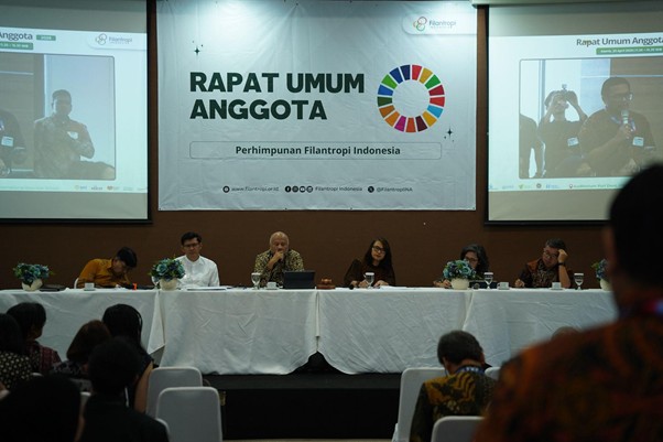 penghargaan penghimpunan filantropi indonesia 8 dompet dhuafa Panel of six people seated at a long white-clothed table on a stage during a conference; a large banner behind reads 'RAPAT UMUM ANGGOTA' with a colorful circular logo and 'Perhimpunan Filantropi Indonesia'.