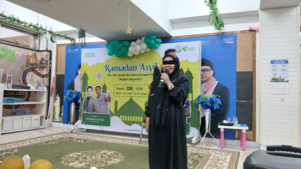 ramadan asyik kb ra istiqlal 3 dompet dhuafa Woman in a black abaya speaks into a microphone on a stage with a Ramadan-themed banner and teal/white balloons behind her.