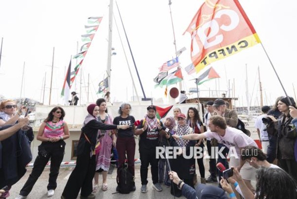 republika gsf gaza 2026 1 dompet dhuafa Diverse group of people on a marina pier waving colorful flags and posing for photos, with sailboats in the background.