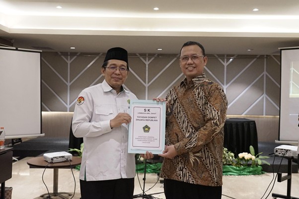 sk laz 2026 1 dompet dhuafa Two men stand on a stage exchanging a framed certificate during a formal awards ceremony in a conference room.