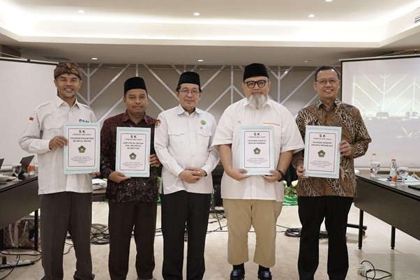 sk laz 2026 8 dompet dhuafa Six men stand side by side in a ceremony, each holding a framed certificate, in a room with presentation screens and a long table behind them.