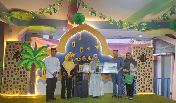 zakat fitrah sekolah embun pagi 1 dompet dhuafa Six people stand on a festively lit stage, holding certificates and a donation check, with an arched backdrop, lanterns, and green garlands in the background.