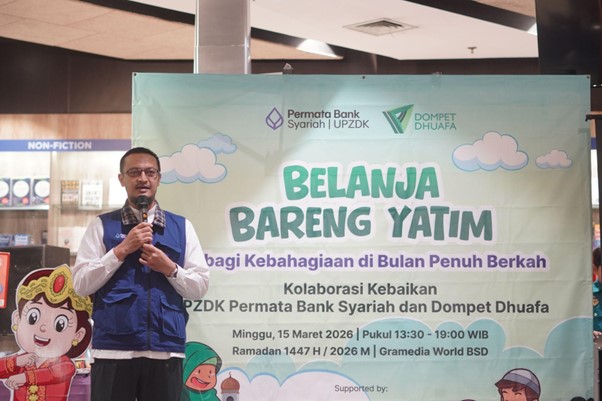 50anakyatimbelanjagramediabsd01 dompet dhuafa Man in a blue vest speaks into a microphone on a stage beside a large banner for the 'Belanja Bareng Yatim' charity event.