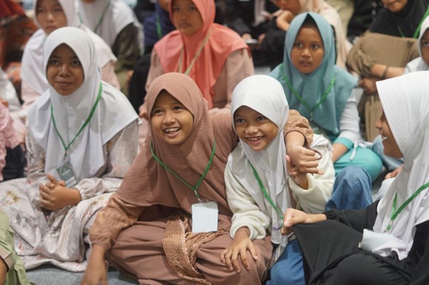 50anakyatimbelanjagramediabsd02 dompet dhuafa Group of smiling young girls wearing hijabs and green lanyards, seated together at an event.”