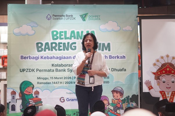 50anakyatimbelanjagramediabsd07 dompet dhuafa Woman with a microphone speaking on a stage in front of a banner for a community event titled Belanja Bareng Umum, collaboration by Permata Bank Syariah and UPDZK/Dhufafta (Ramadan 1447H)