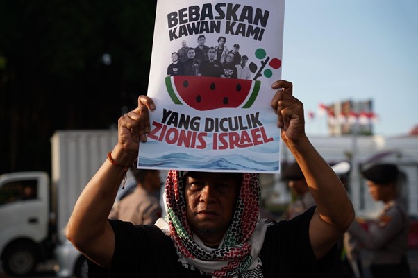 9 wni bebas dari israel 1 dompet dhuafa Protester holding a sign that reads 'Bebaskan kawanku yang diculik Zionis Israel' with a watermelon graphic and crowd in the background.
