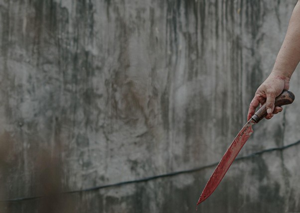 adhapengorbanan3 dompet dhuafa Hand holding a red-bladed knife against a gray, weathered wall.