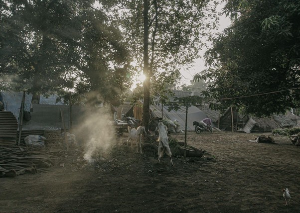 adhapengorbanan5 dompet dhuafa People in white protective suits tending a small fire in a rustic camp with tents and trees at sunset/dusk.