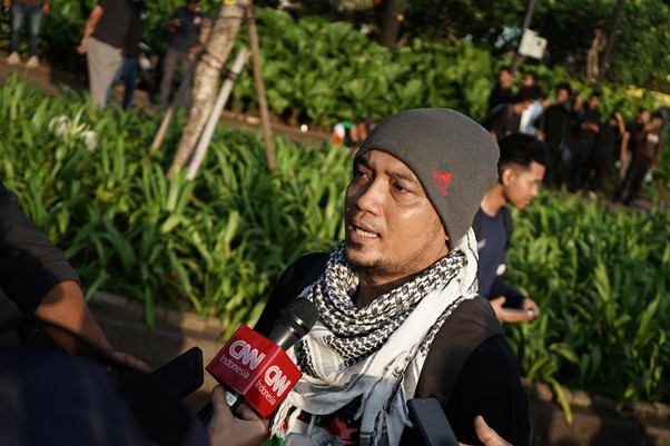 aksi kamisan pembebasan relawan gsf 2 dompet dhuafa Man in a gray beanie and scarf being interviewed outdoors, CNN Indonesia microphone in view.