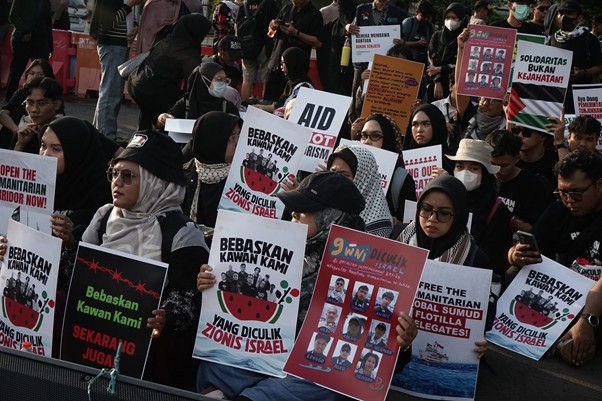 aksi kamisan pembebasan relawan gsf 5 dompet dhuafa Crowd of protesters at an outdoor rally, many wearing headscarves and masks, holding Indonesian placards demanding freedom for detained peers and criticizing Israel.