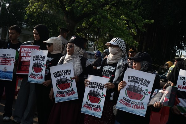 aksi kamisan pembebasan relawan gsf 7 dompet dhuafa A group of protesters outdoors, many wearing hijabs, holding posters that say 'Bebaskan Kawan Kami Yang Diculik Zionis Israel' in support of freeing kidnapped comrades.