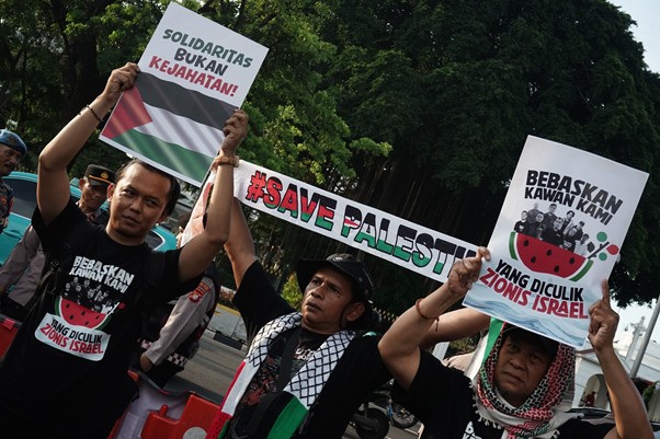 aksi kamisan pembebasan relawan gsf 8 dompet dhuafa Protesters raise signs and a large 'Save Palestine' banner at a street rally, some wearing keffiyehs and black T-shirts.