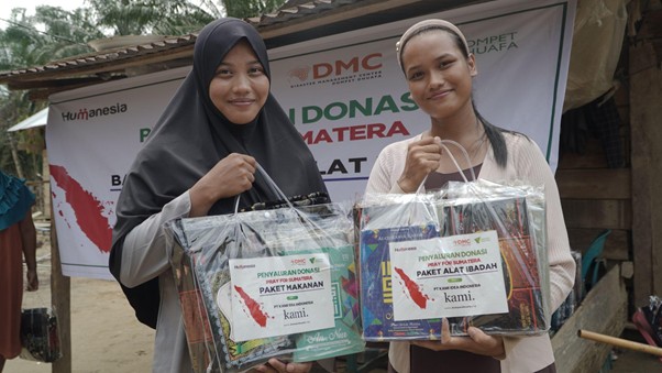 bantuankamiideaaceh6 dompet dhuafa Two smiling women in headscarves hold plastic-wrapped donation packages outdoors, in front of a charity banner.