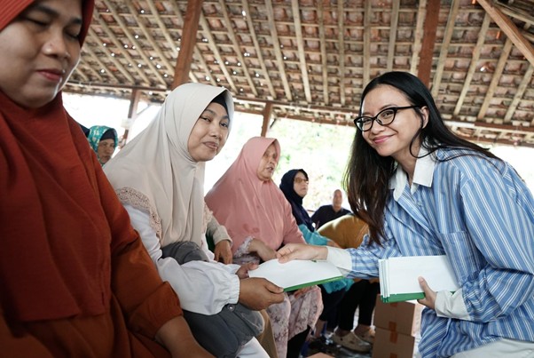 bantuanmodenauntukibuibutunanetra4 dompet dhuafa A woman in a striped blue shirt hands a document to a woman wearing a hijab at a community event, others seated nearby.
