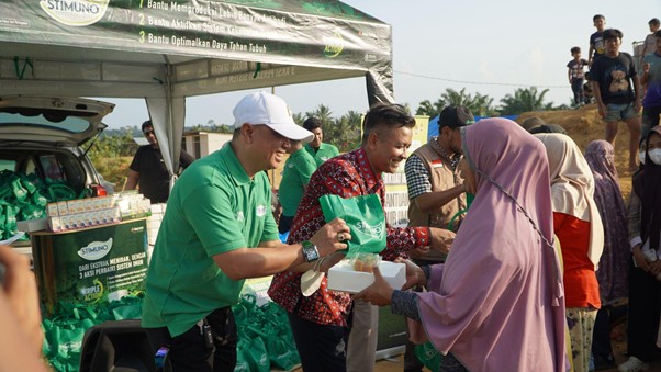 bantuanstimunountukacehtamiang3 dompet dhuafa Volunteer in a green shirt and white cap hands a green bag to a woman in a hijab at a donation event under a canopy.