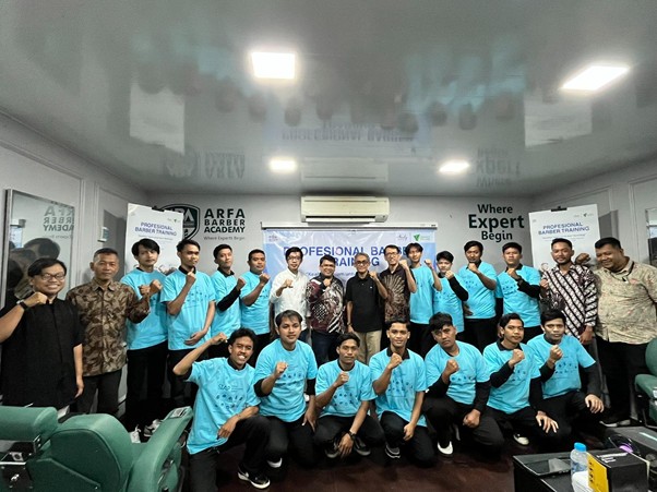 Group photo of students and instructors at a barber training academy, many in turquoise shirts, posing with thumbs up.