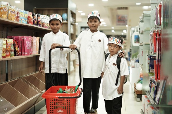 belanjabarengyatimparagon4 dompet dhuafa Three boys in white shirts and caps stand in a grocery store aisle with a red shopping basket to push or hold eruption?