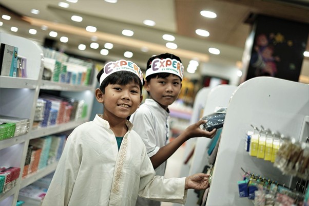 belanjabarengyatimparagon6 dompet dhuafa Two young boys wearing explorer hats browse a bright store aisle in a retail shop.