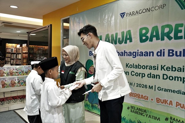belanjabarengyatimparagon8 dompet dhuafa Man in a white shirt hands a certificate to a young boy in a white outfit at a charity event, with a woman in a hijab nearby and a banner in Indonesian in the background.
