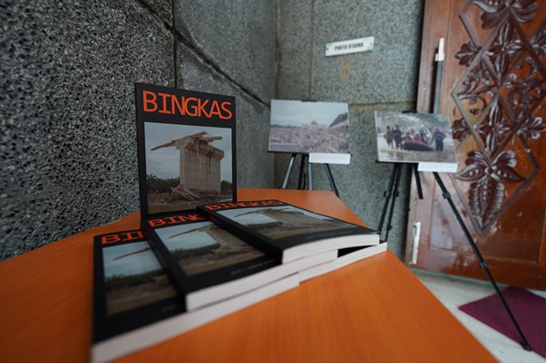 bukufotobingkas5 dompet dhuafa Table with several copies of the book 'BINGKAS' displayed; photo boards on stands are visible in the background near a stone wall and an ornate wooden door.