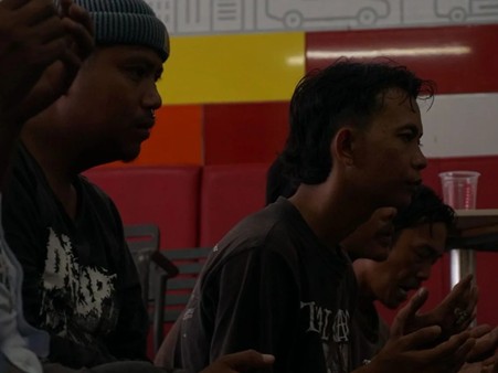 dakwahinklusifcordofa3 dompet dhuafa Three young men sit in a dimly lit room with a colorful wall behind them, appearing to talk.