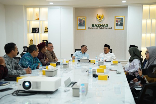 Group of Indonesian officials seated around a long conference table in a bright meeting room at BAZNAS, engaged in discussion with a projector at the front.
