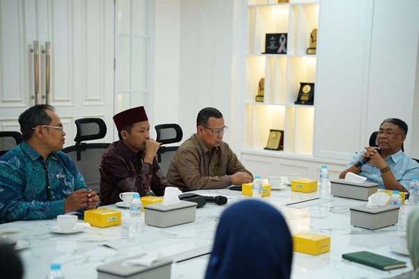 Five men sit around a marble conference table in a bright, modern room, mid-discussion with notebooks and tissues on the table and award shelves in the background.