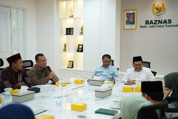 Five men seated around a white marble conference table during a BAZNAS meeting, with boxes, water bottles, and a laptop on the table.