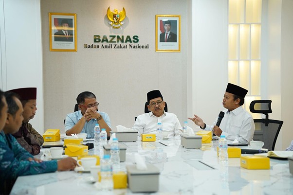 Panel of men around a conference table during a BAZNAS meeting, with the national emblem on the wall behind them