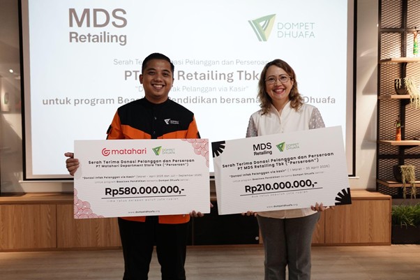 donasi mds retailing dompet dhuafa Two smiling recipients stand side by side, each holding an oversized donation check (Rp580,000,000 and Rp210,000,000) during a presentation, with a screen showing MDS Retailing and Dompet Dhuafa logos in the background.