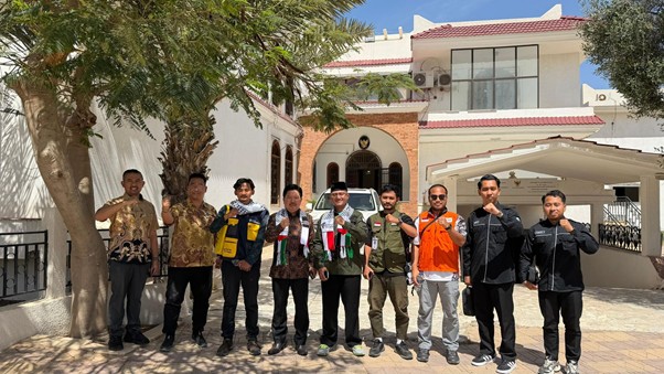 gsf 20 jalur darat 1 dompet dhuafa Ten men stand in a line outside a white building with an arched entrance, many wearing vests or jackets, and all giving a thumbs up at the camera.