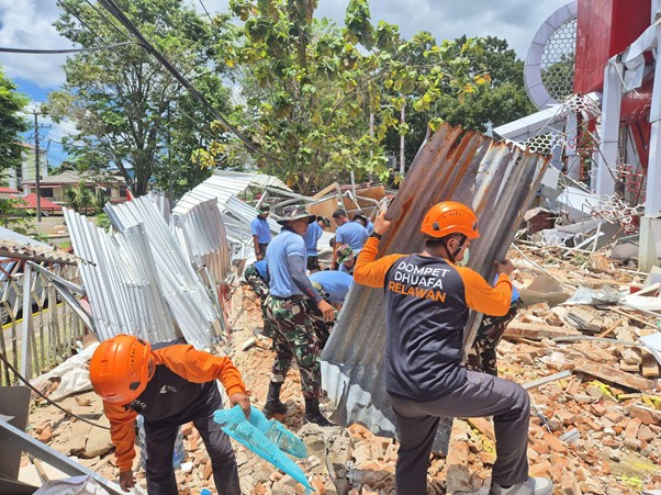 gempasulawesidanmalut20262 dompet dhuafa Rescue volunteers in orange helmets clear corrugated metal and rubble at a collapsed building site.