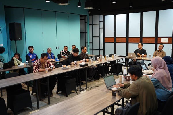 Group of people seated around long tables in a modern conference room, many with laptops open