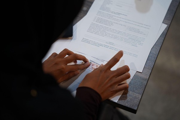 Person's hands rest on documents as they are signed or stamped at a desk view from above on papers laid out.