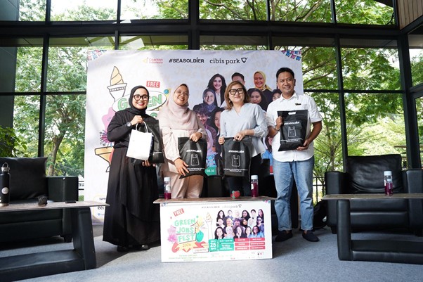 greenjobsdanekonomihijau5 dompet dhuafa Seven people pose on a stage, each holding black gift bags, at a Green Jobs Fest event with a banner behind them.