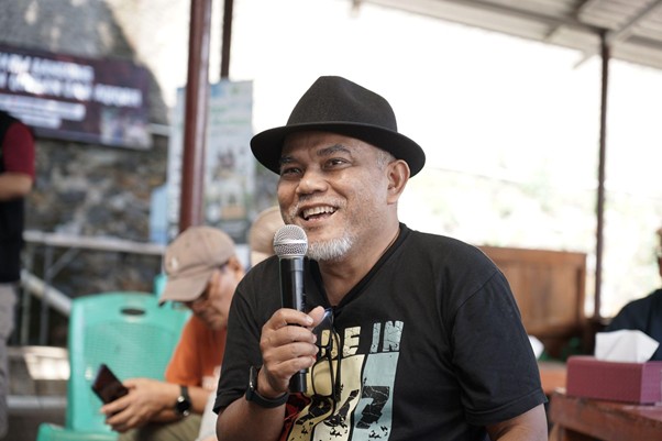 jelajahkandanguntukkurban20265 dompet dhuafa Smiling man wearing a black fedora speaks into a handheld microphone at an outdoor event.