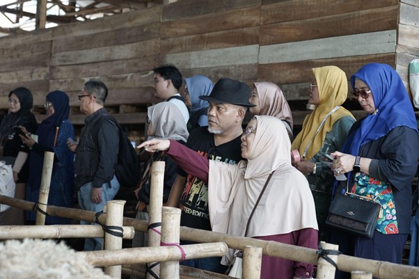 jelajahkandanguntukkurban20266 dompet dhuafa Group of diverse adults in hijabs and casual clothing watch an exhibit behind a wooden railing; a man in a hat points toward something ahead.