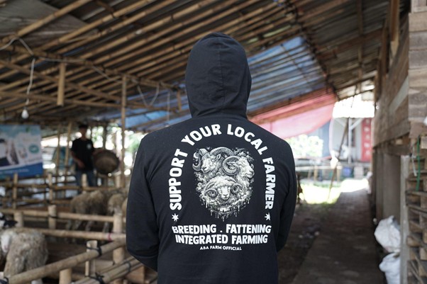 jelajahkandanguntukkurban20269 dompet dhuafa Person wearing a black hoodie with the slogan 'Support Your Local Farmer' on the back, standing in a farm barn.