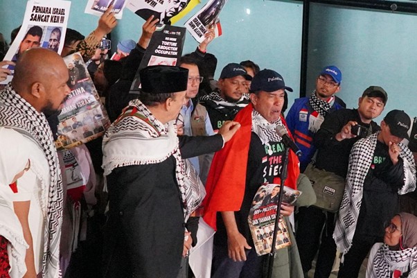 kedatangan delegasi gsf 20 1 dompet dhuafa Group of protesters wearing keffiyeh scarves, holding posters, and one man in a red scarf speaks into a microphone to the crowd.