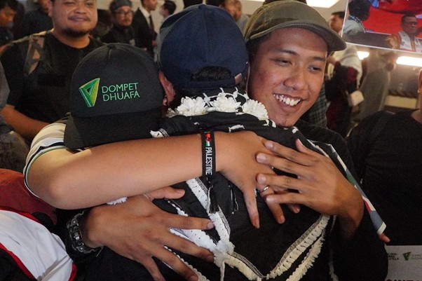 kedatangan delegasi gsf 20 5 dompet dhuafa Two men embrace in a crowded room; one wears a black cap with the Dompet Dhuafa logo and a white flower lei.