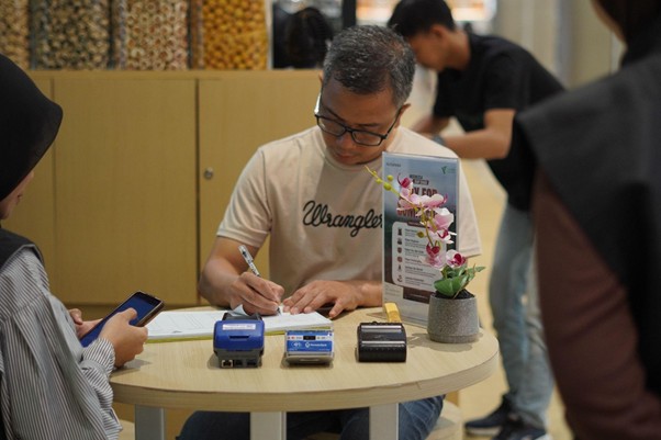 Man in a beige Wrangler shirt signs a form at a round table, with card readers and a small plant nearby in a store setting
