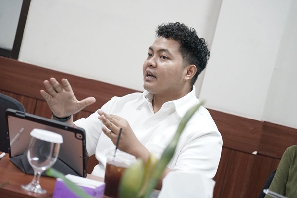 kolaborasimarcellazalianty6 dompet dhuafa Man in a white shirt speaks and gestures while seated at a conference table with a tablet in front of him.