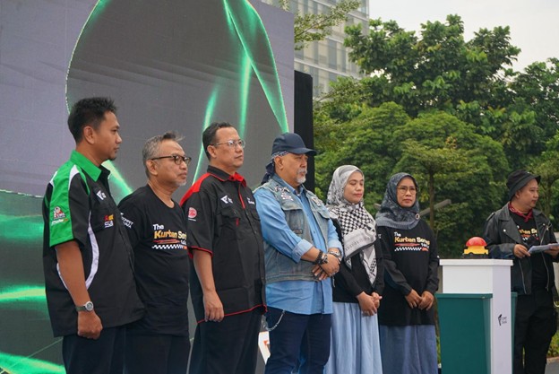 kurbanaval 2026 1 dompet dhuafa Group of eight adults standing in a row on an outdoor stage during a ceremony, with a large screen and trees in the background.