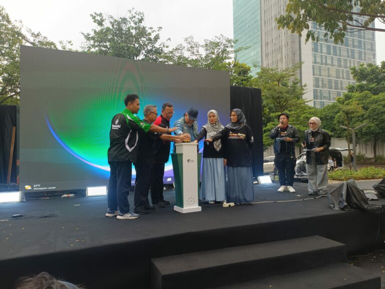 kurbanavalthekurbanseries1447h2768x576 dompet dhuafa Group of diverse people on an outdoor stage placing their hands on a podium during a launch ceremony with a large screen behind them.